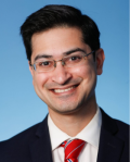 a middle aged man with glasses and short black hair wearing a suit