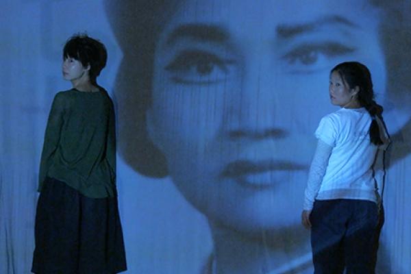 picture of two people in front with large woman's face in background from film
